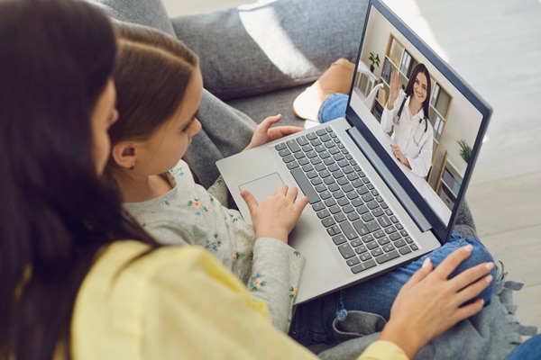 Family doctor online. Mom and little girl daughter are at home and use a video call to receive medical care online. Family doctor woman on laptop screen gives medical advice on the Internet. Telemedicine concept.