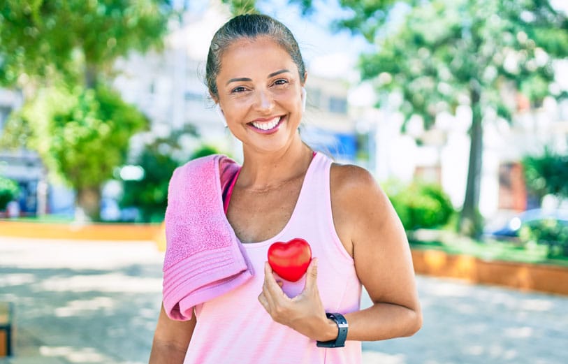 Middle age sportswoman asking for health care holding heart at the park