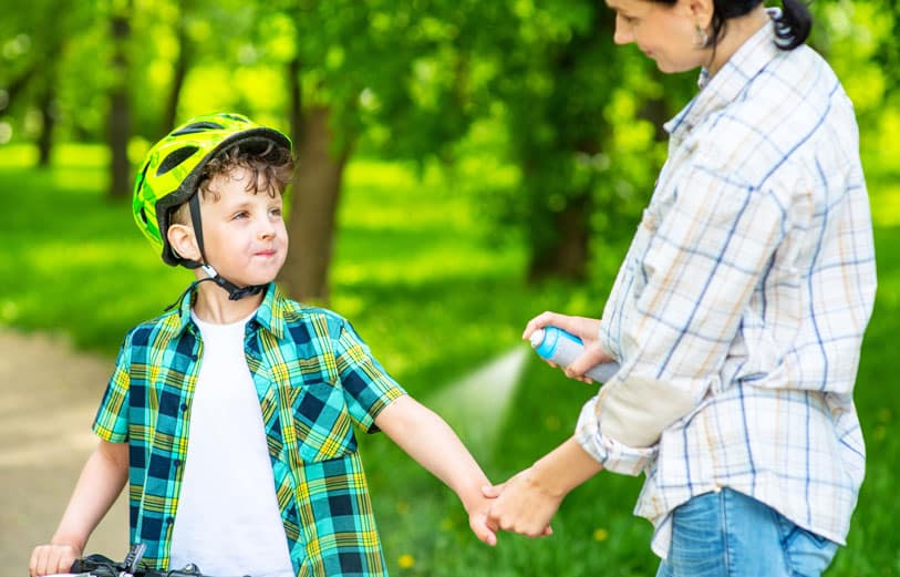 Mother applying spray on bug spray to son's arm.