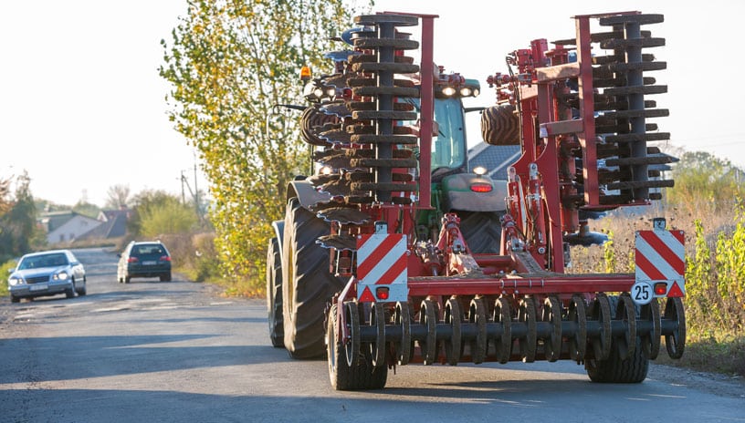 Farm equipment driving down the road with traffic stopped.