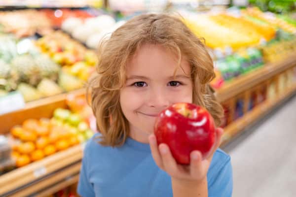 Portrait of child with shopping cart full of fresh vegetables in a food store. Supermarket shopping and grocery shop concept. Shopping kids. Child buying grocery in supermarket. hold shopping basket.