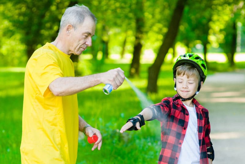 Man spraying child with bug spray