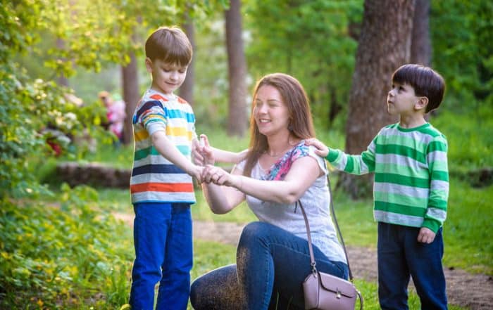 Woman spraying children with bug spray to prevent mosquito bites.
