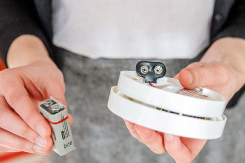 Person installing new battery into smoke detector