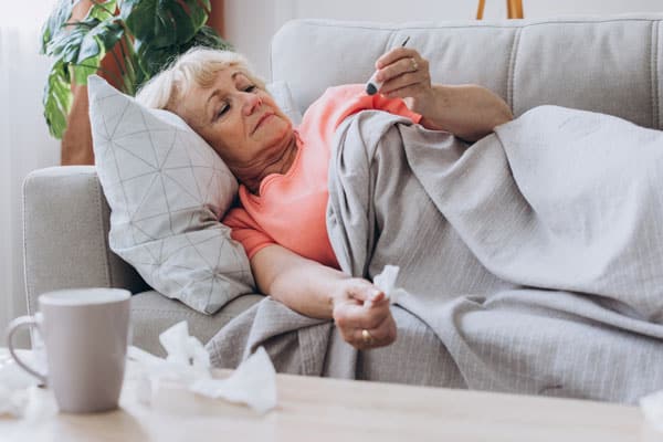 Mature woman holding thermometer while lying on sofa at home