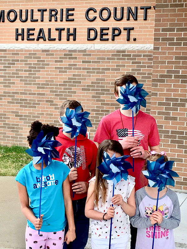 children holding blue pinwheels in front of their faces for Child Abuse Awareness Month