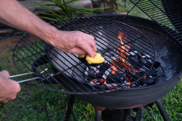 A closeup shot of a person cleaning a rack with a cloth on a grill