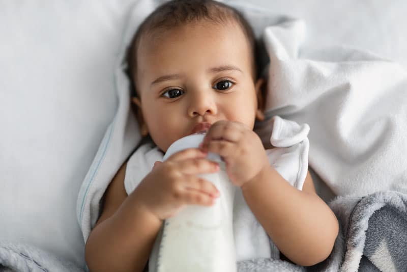 cute little african american child drinking from bottle