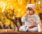 Baby sitting on table with fall leaves and trees behind her