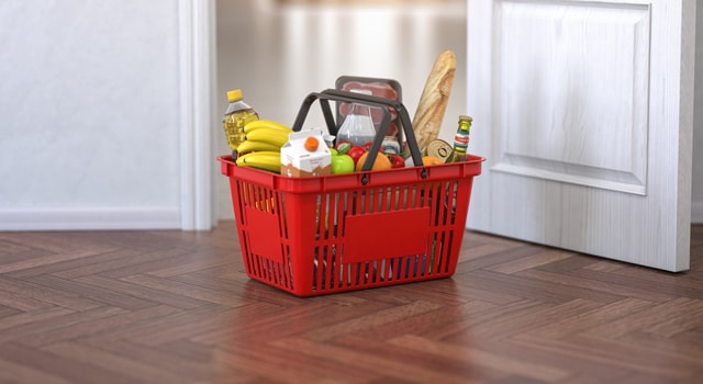 red shopping basket full of groceries sitting inside a doorway