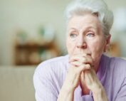 elderly woman looking into the distance with hands folded near her face