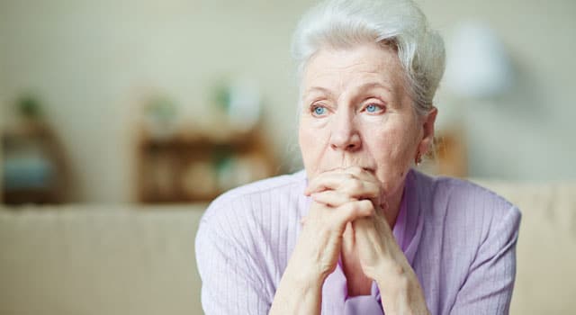 elderly woman looking into the distance with hands folded near her face