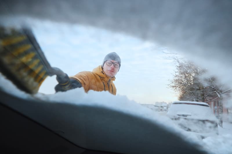 man clearing snow from windshield of his car