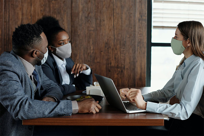 three people having a meeting wearing masks