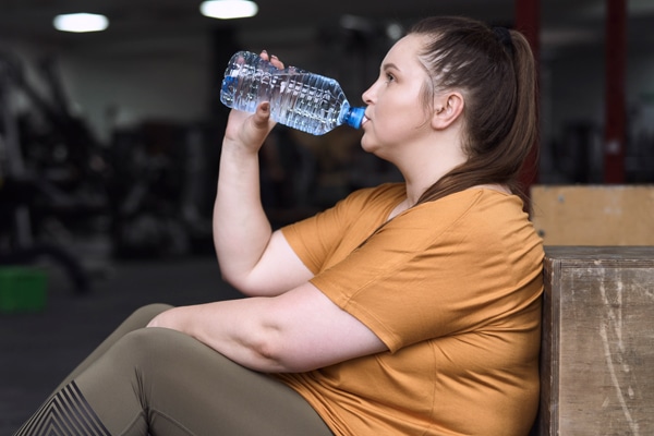 overweight tired woman drinking water at the gym