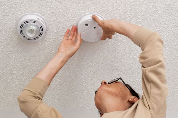 Woman reaching up for smoke alarm on ceiling at home