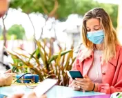 woman using mobile phone while wearing a mask sitting outdoors