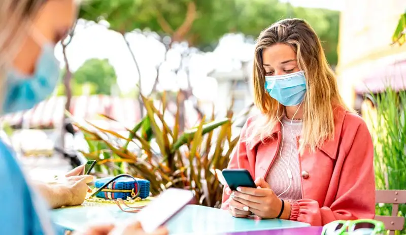woman using mobile phone while wearing a mask sitting outdoors woman using mobile phone while wearing a mask sitting outdoors